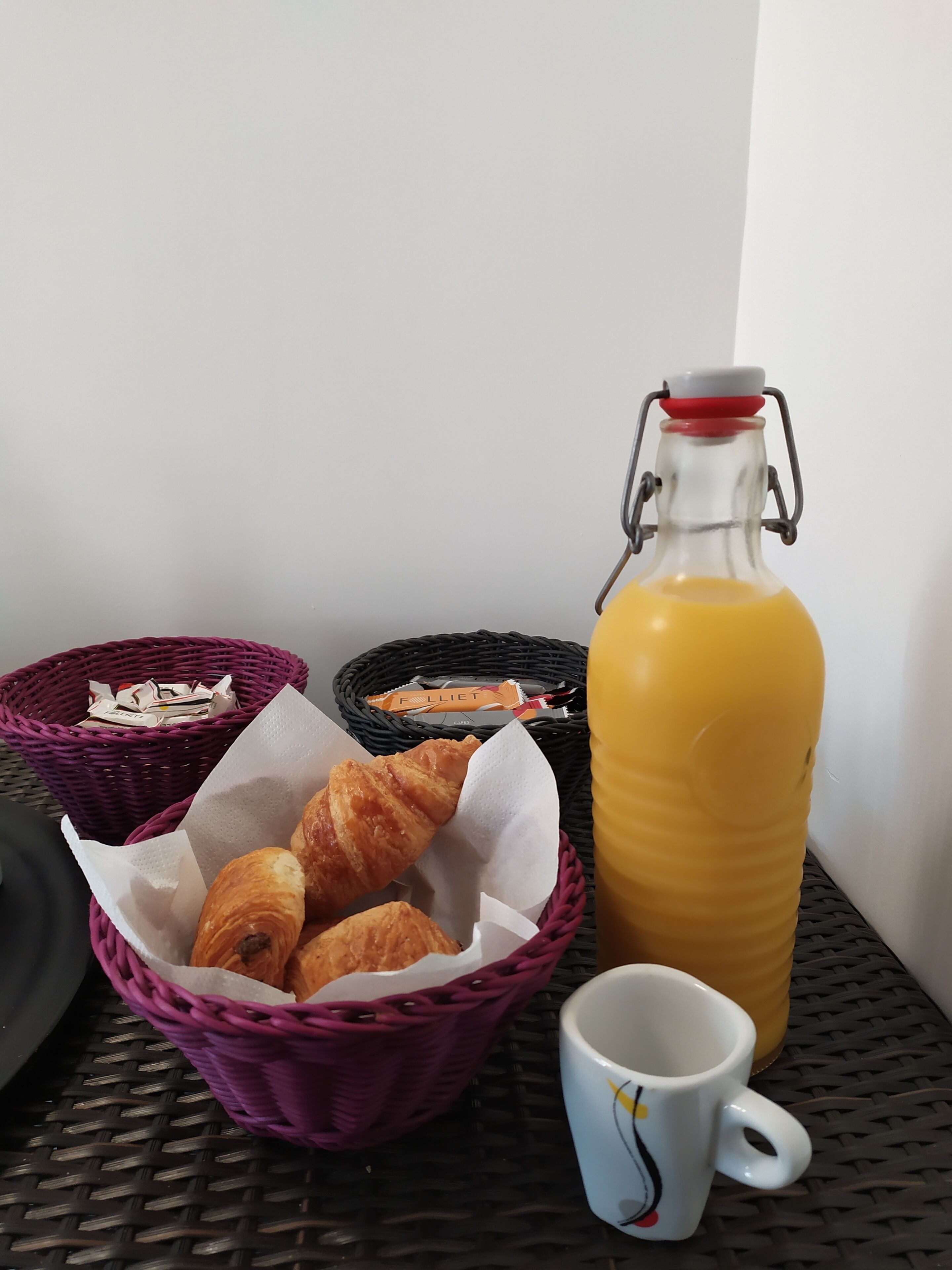 Ein Frühstückstisch mit Croissants, einer Orangensaftflasche und einer Tasse auf einer gewebten Tischdecke.