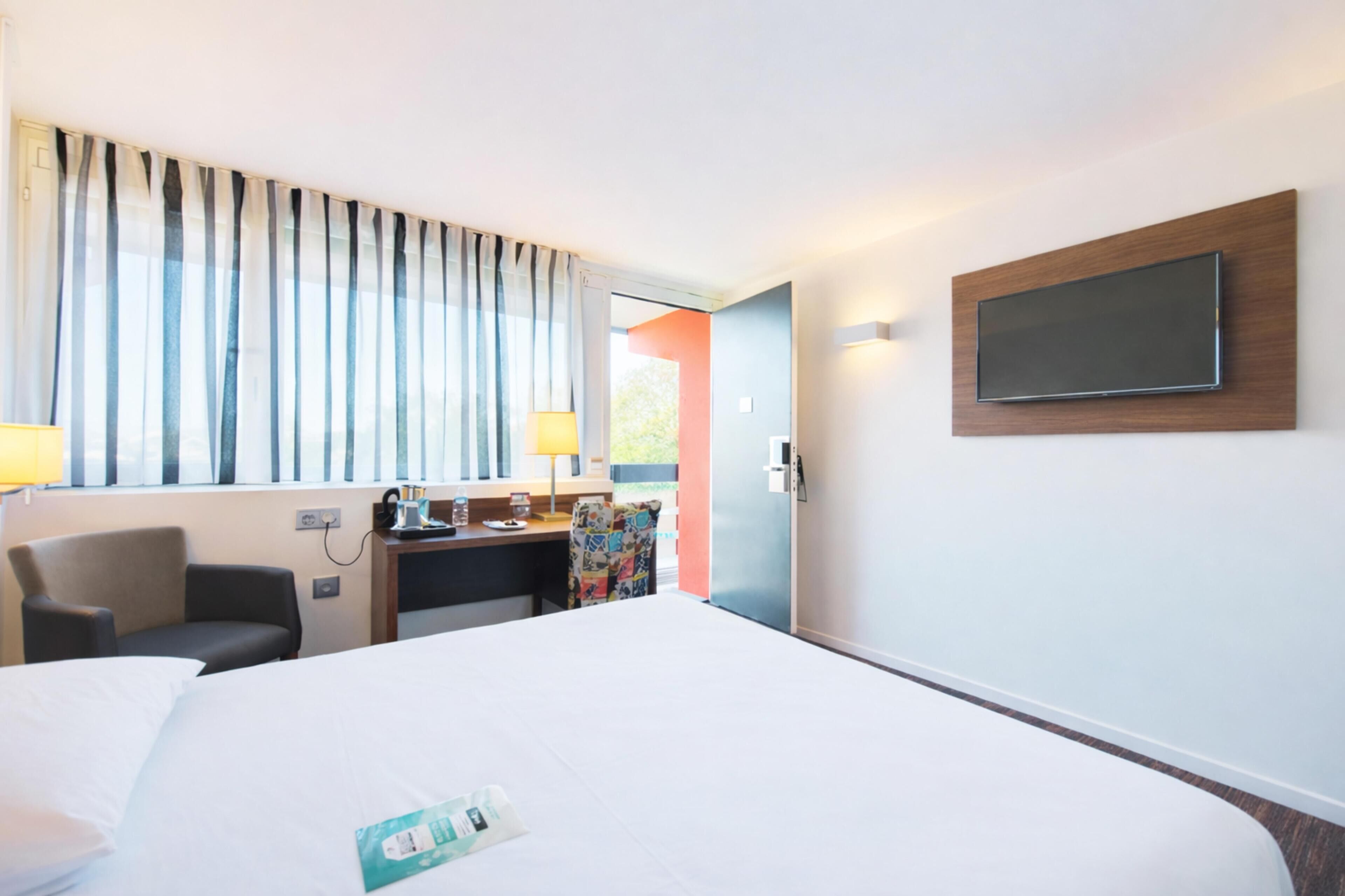 Une chambre d’hôtel avec un grand lit, un bureau avec une lampe, une chaise et un téléviseur fixé au mur.