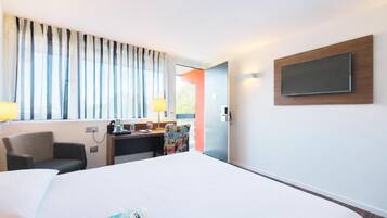 Une chambre d’hôtel avec un grand lit, un bureau avec une lampe, une chaise et un téléviseur fixé au mur.