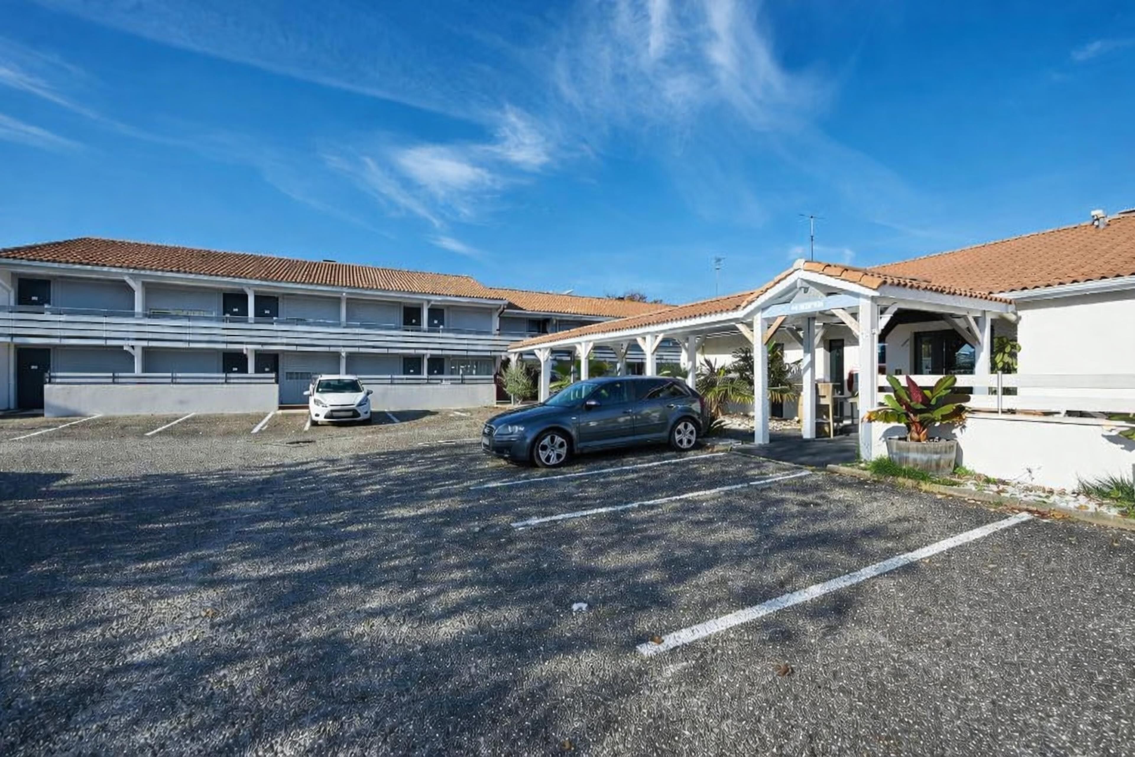 A building with a parking lot, a covered area, and a car parked in the lot.