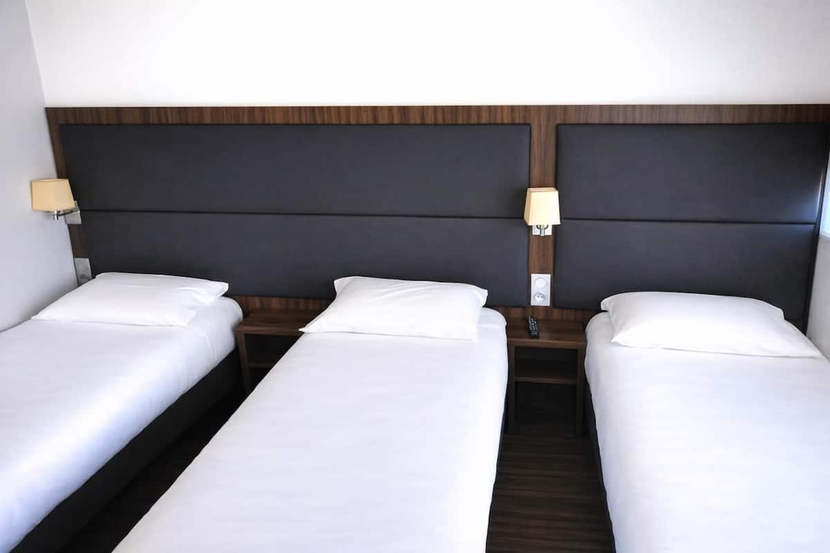 Une chambre d’hôtel avec trois lits simples, chacun doté d’une tête de lit en bois et de lampes de chevet.