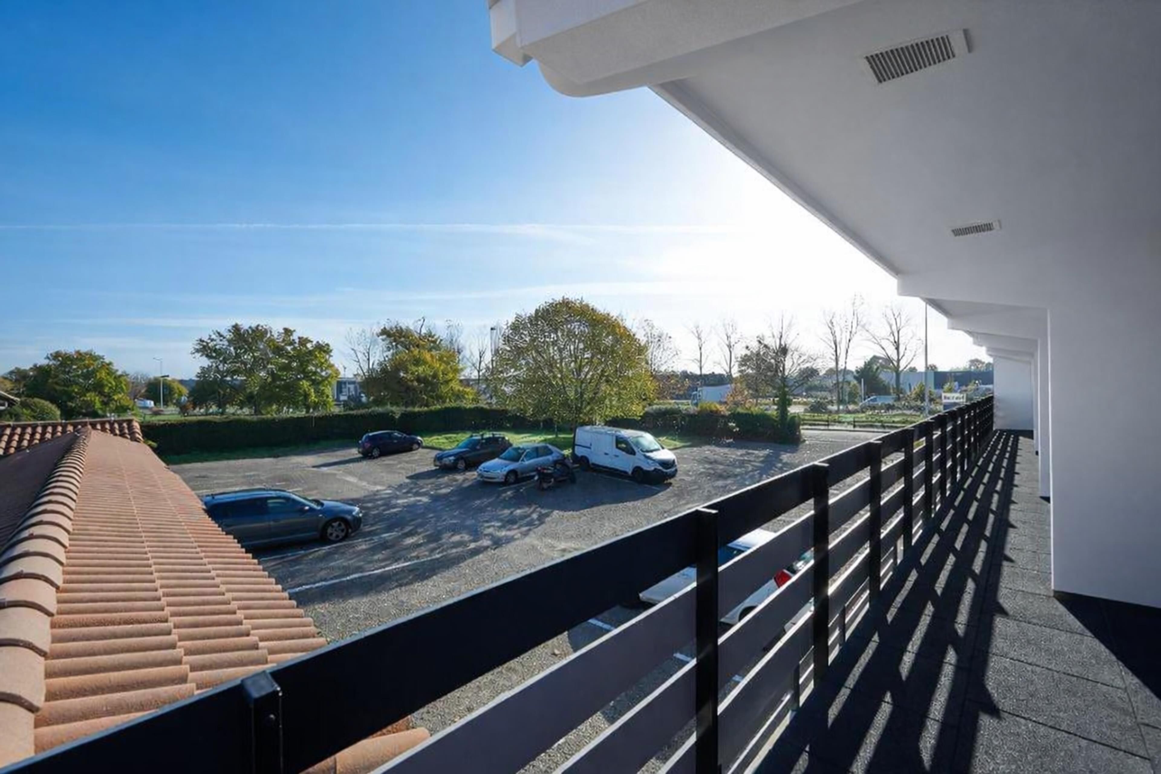 A balcony with a view of a parking lot and trees.