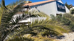 A building with a sign reading "Kyriad" and a palm tree in the foreground. - Kyriad Bordeaux - Mérignac Aéroport (Merignac)