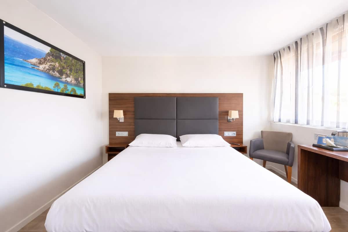 Une chambre d’hôtel avec un grand lit, un bureau, une chaise et un tableau au mur.