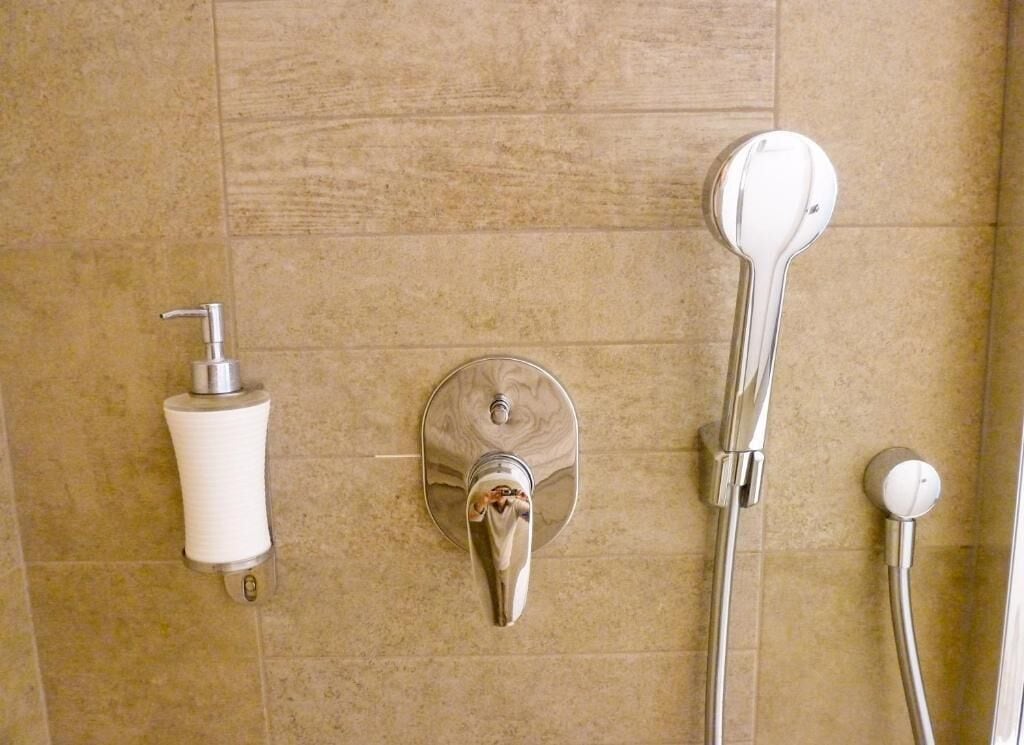 Un baño con ducha, un dispensador de papel higiénico y un grifo.