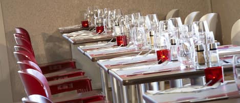 A conference room with rows of tables, each equipped with glassware and red candle holders.