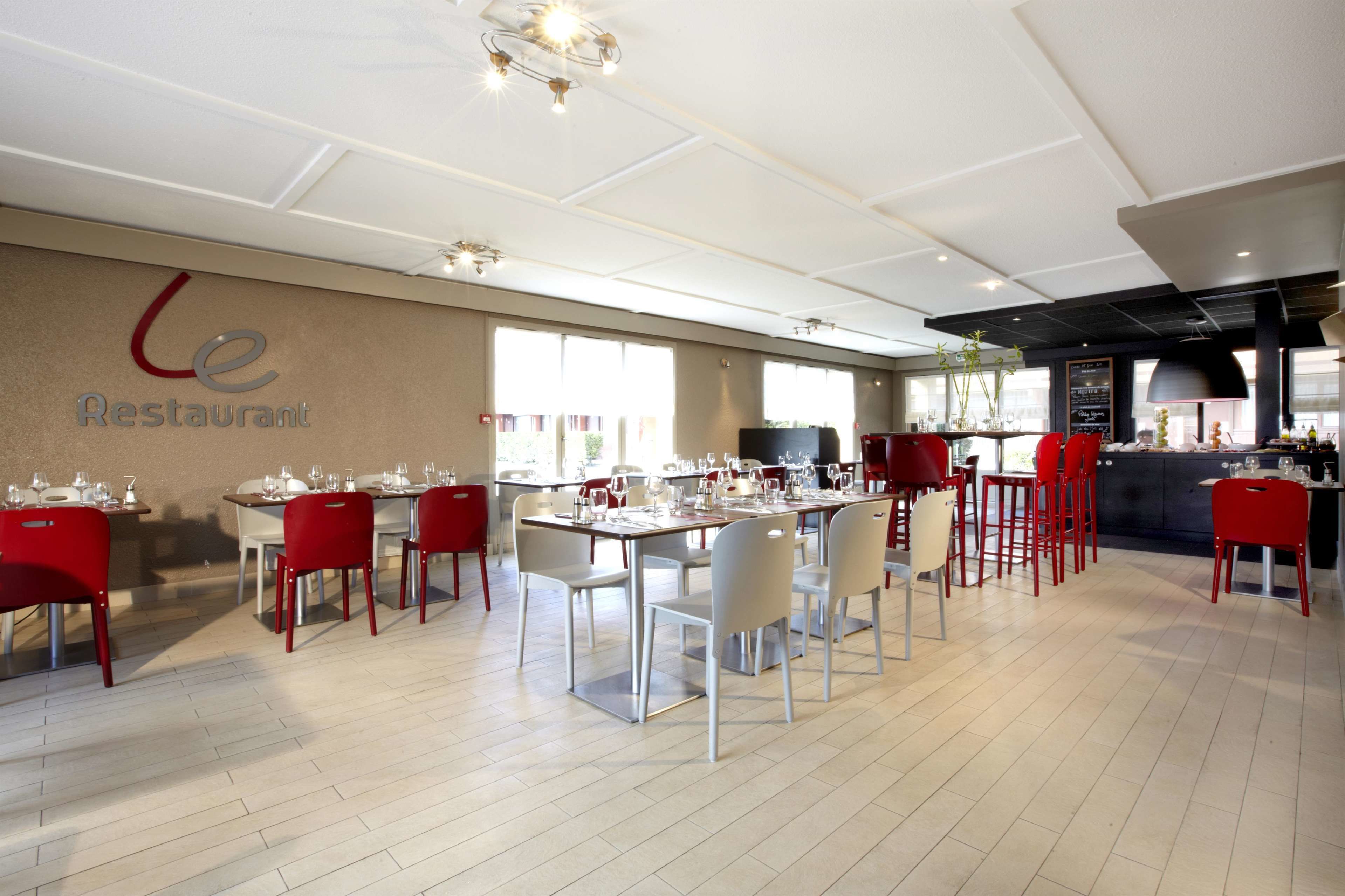 A restaurant with multiple dining tables and chairs, a kitchen area, and a view of the outdoors.
