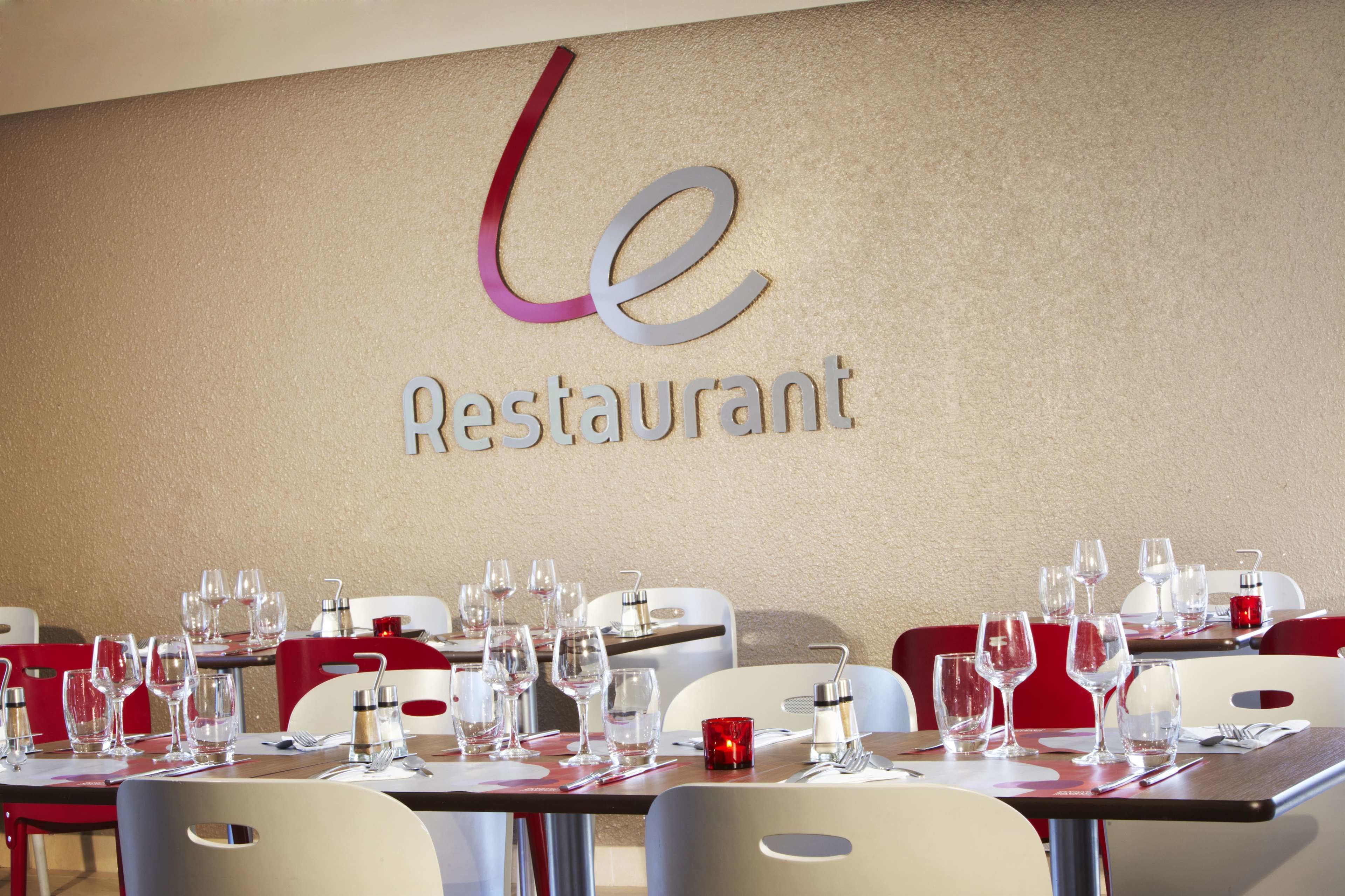A restaurant with a modern interior, featuring tables set with wine glasses and cutlery, and a prominent logo on the wall.