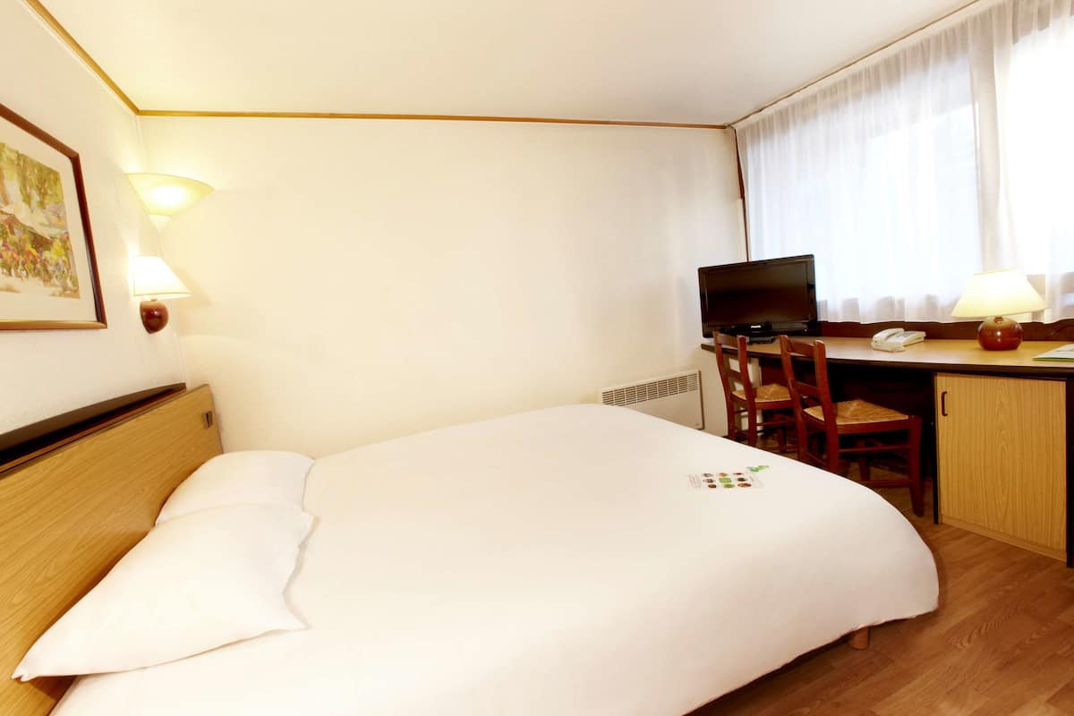 A hotel room with a bed, desk, chair, and a television.