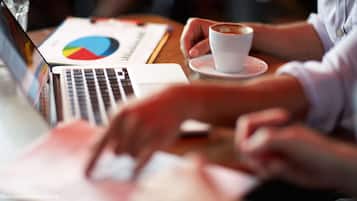 A laptop, a pie chart, and a cup of coffee on a table.