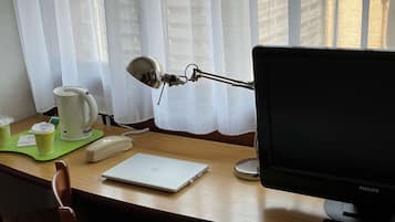 Een houten bureau met een laptop, een telefoon, een koffiezetapparaat en een bureaulamp.
