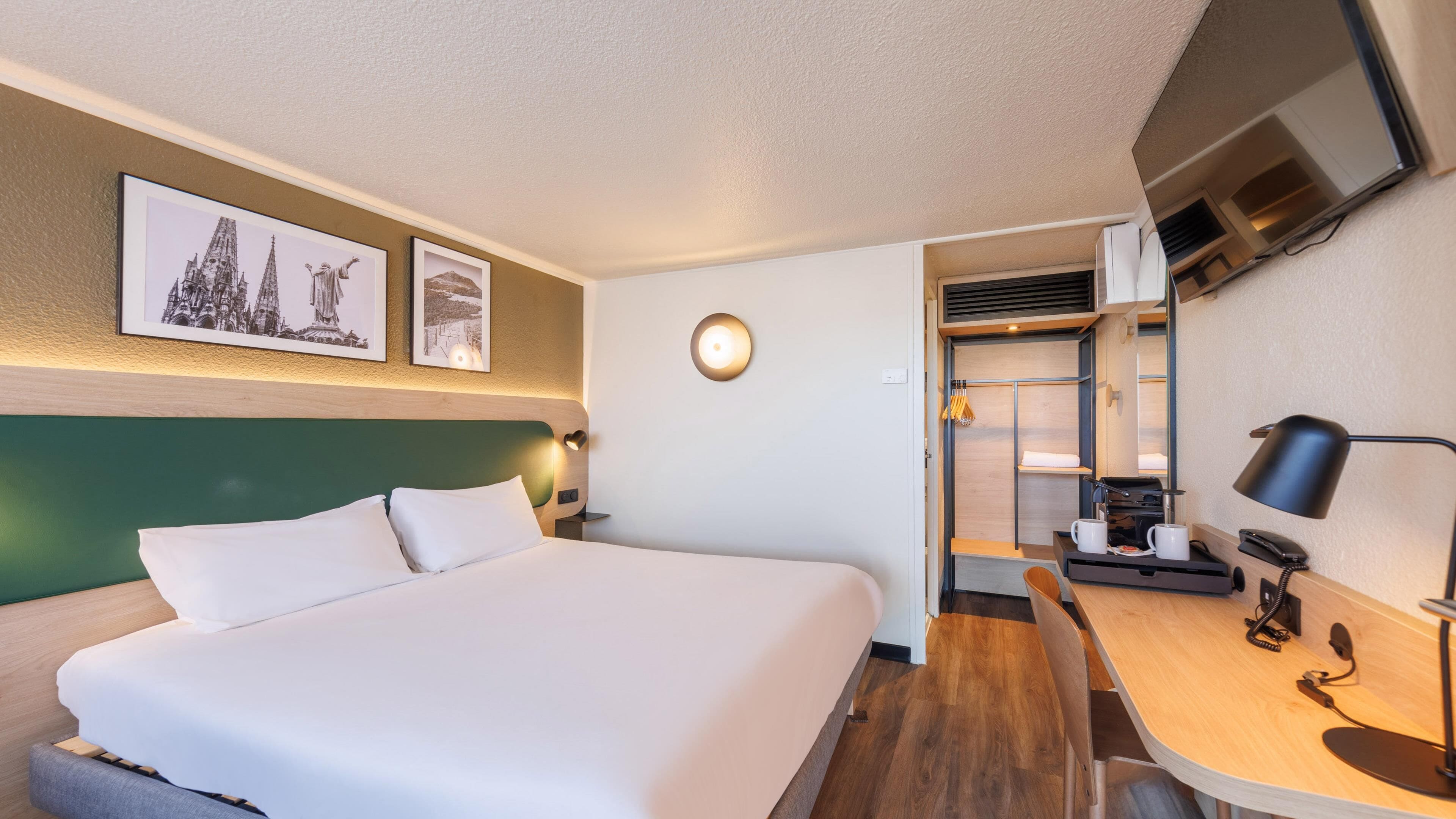 A hotel room with a bed, desk, chair, and a small kitchenette.