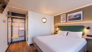 Ein Hotelzimmer mit Bett, Kleiderschrank, Wandleuchte und zwei gerahmten Bildern.