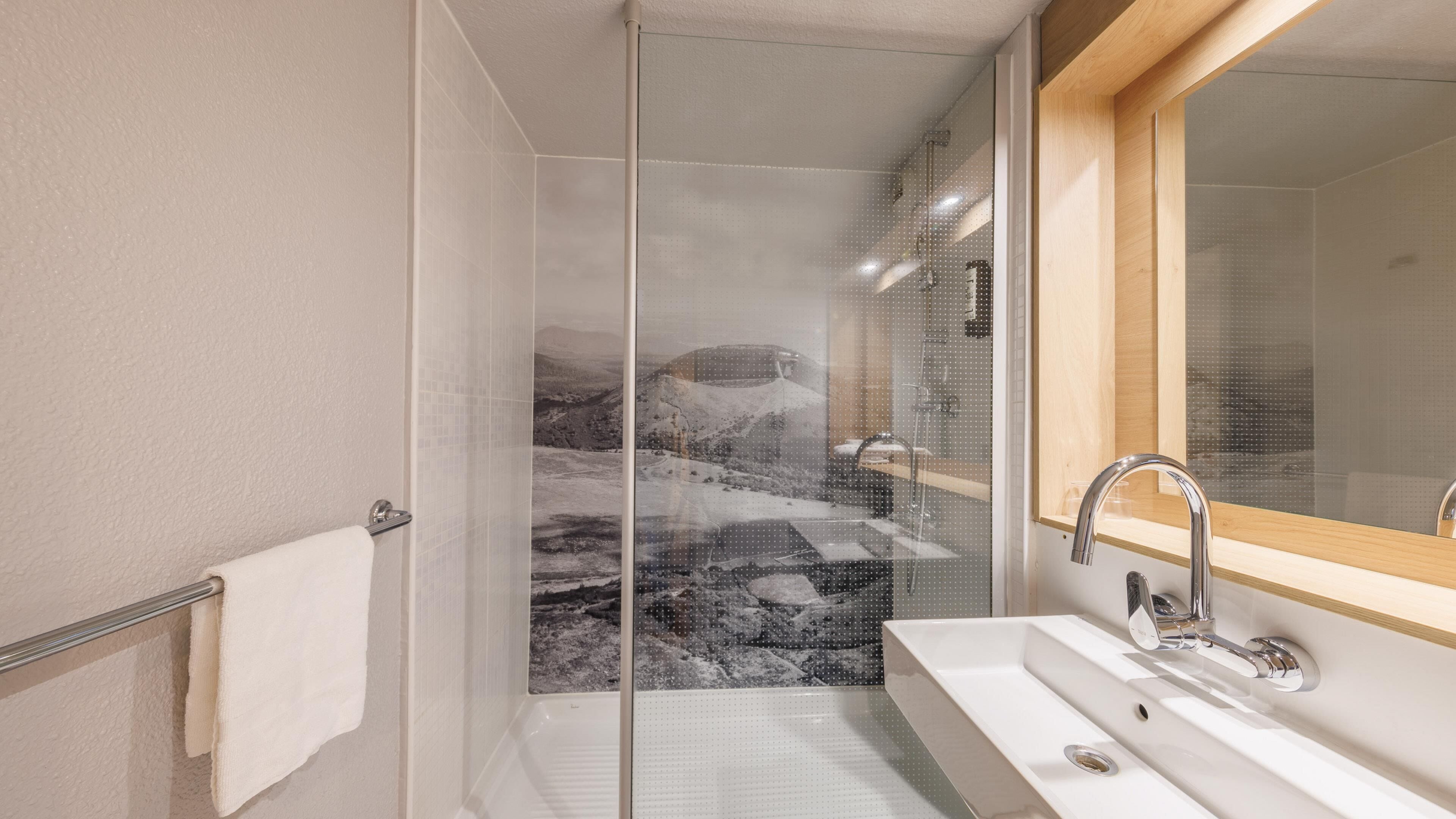 Un baño moderno con cabina de ducha de cristal, un lavabo blanco y un espejo con marco de madera.