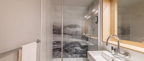 Un baño moderno con cabina de ducha de cristal, un lavabo blanco y un espejo con marco de madera.
