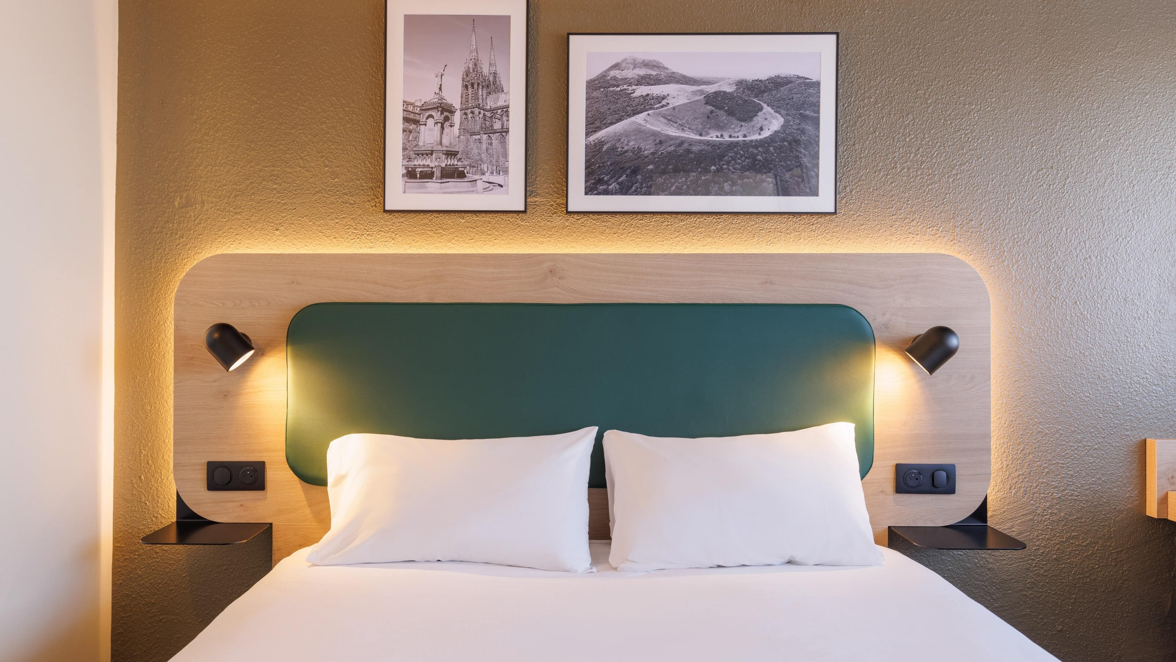 Habitación de hotel con cama, dos mesitas de noche, cabecera verde y dos cuadros en la pared.