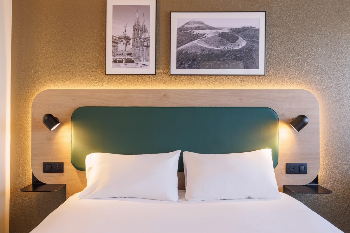 Ein Hotelzimmer mit einem Bett, zwei Nachttischen, einem grünen Kopfteil und zwei gerahmten Bildern an der Wand.