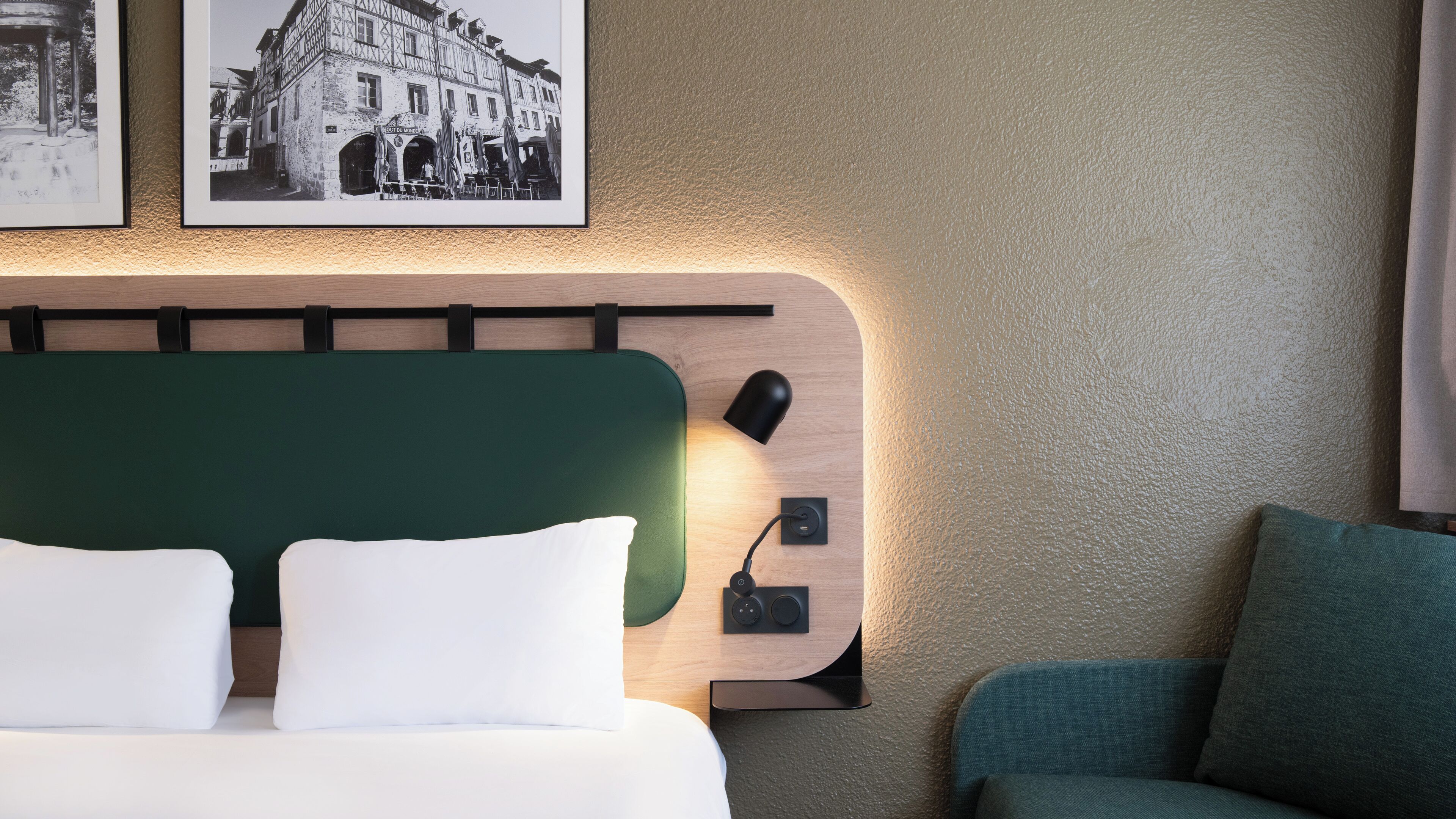 Una habitación de hotel con cabecera verde, una lámpara de noche y una fotografía en blanco y negro enmarcada en la pared.