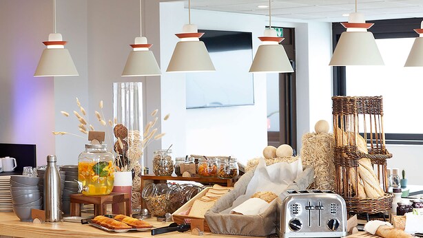 A breakfast buffet with various food items, a toaster, and hanging pendant lights. - Campanile NATURE - Clermont Ferrand Le Brézet (Clermont-Ferrand)