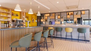 A modern bar area with a bar counter, stools, and shelves with bottles and glasses. - Campanile NATURE - Clermont Ferrand Le Brézet (Clermont-Ferrand)