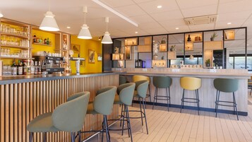 Un moderno bar con barra, taburetes y estanterías llenas de botellas y copas.