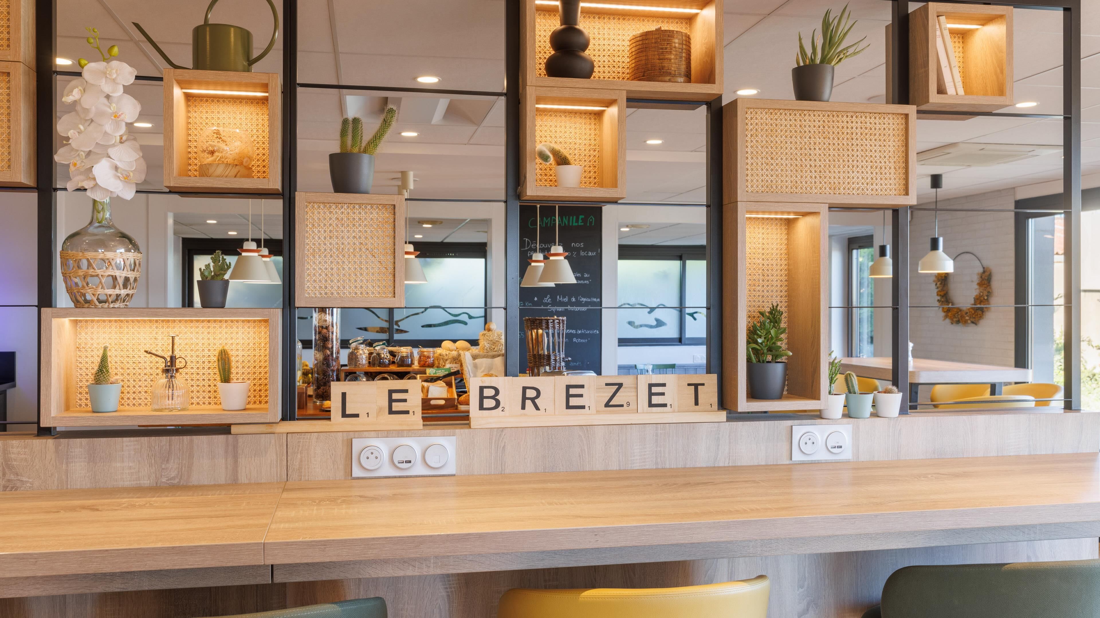 Un mostrador de recepción con estanterías de madera, plantas en macetas y un cartel con la inscripción 'LE BREZET'.