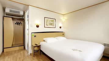 Habitación de hotel con suelo de madera, cama con ropa de cama blanca, mesita de noche, armario y dos lámparas de pared.