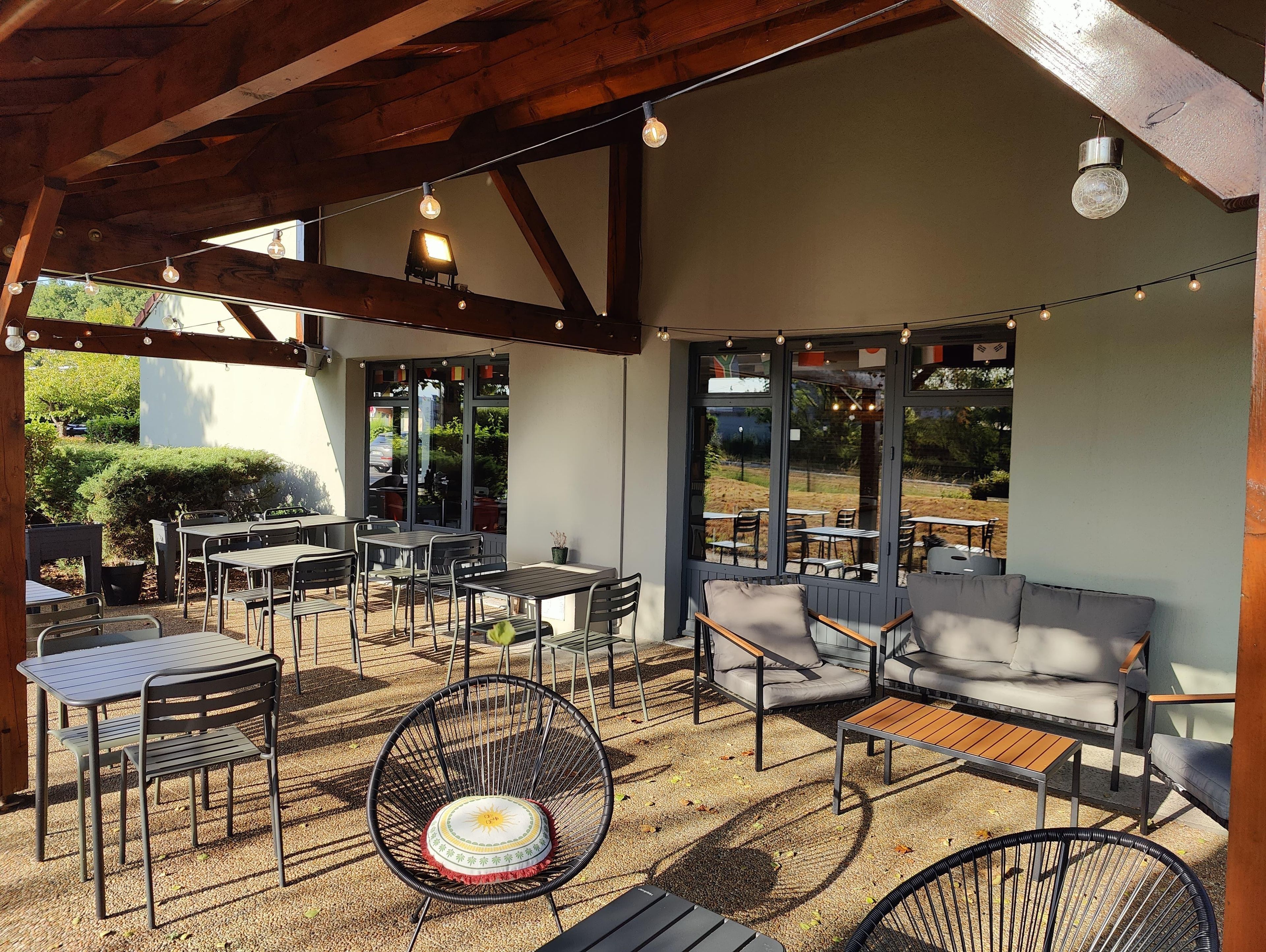 An outdoor seating area with tables, chairs, and a sofa under a wooden structure with string lights.