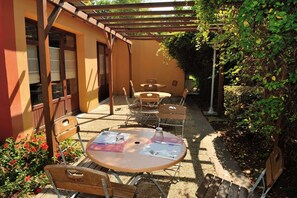 Une terrasse extérieure avec des tables et des chaises en bois, une pergola et un espace jardin agrémenté de plantes et de fleurs.