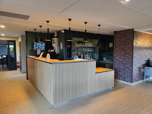 Un espace d’accueil doté d’un comptoir en bois, d’un éclairage suspendu et d’un mur décoratif en briques.