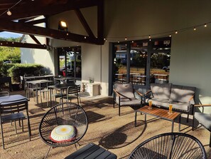 An outdoor patio area with tables, chairs, and a sofa. - Campanile Clermont Thiers (Thiers)