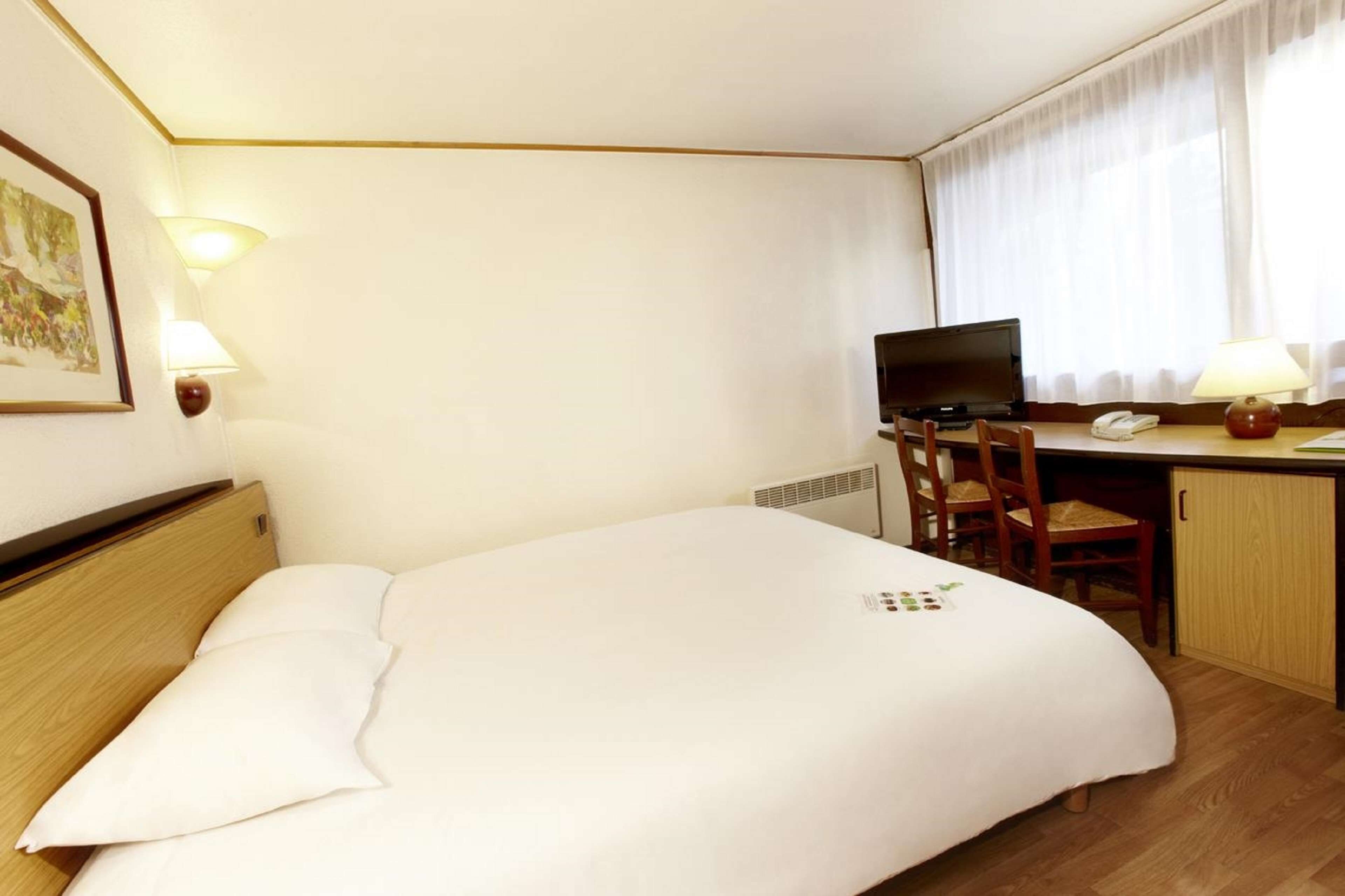 A hotel room with a bed, desk, chair, and a television.