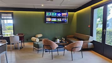 Ein Zimmer mit Fernseher, der Sport zeigt, Sitzgelegenheiten und Blick durch ein Fenster.