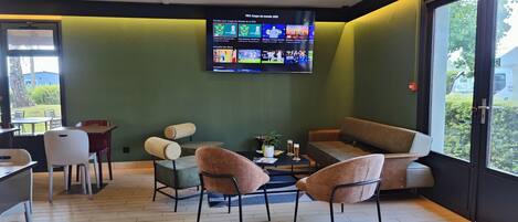 Habitación con televisión mostrando contenido deportivo, disposición de asientos y vistas al exterior.