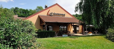 A restaurant with a brown roof and beige walls, surrounded by greenery.
