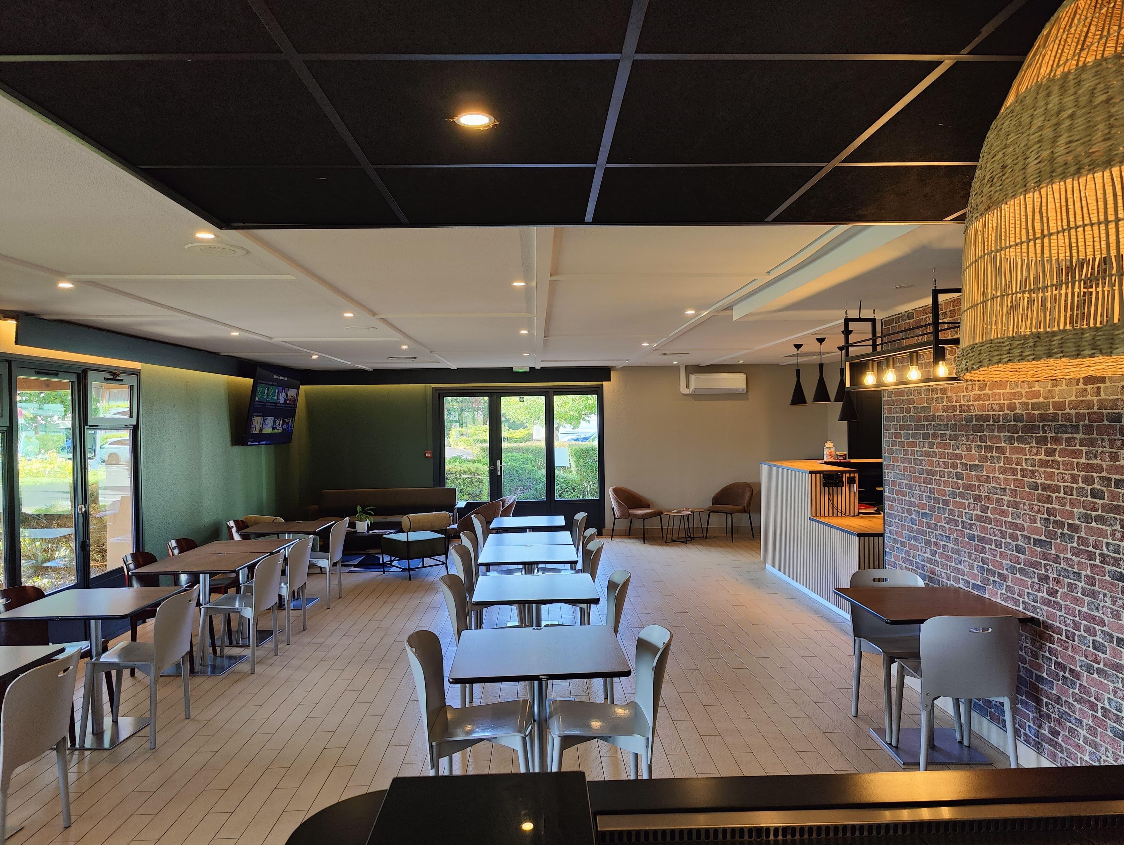 A modern restaurant interior with multiple seating options, including tables and booths, and a brick accent wall.