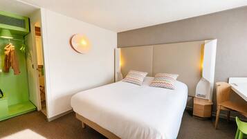 Une chambre d’hôtel équipée d’un lit, d’un bureau, d’une chaise, d’une armoire et d’une lampe fixée au mur.