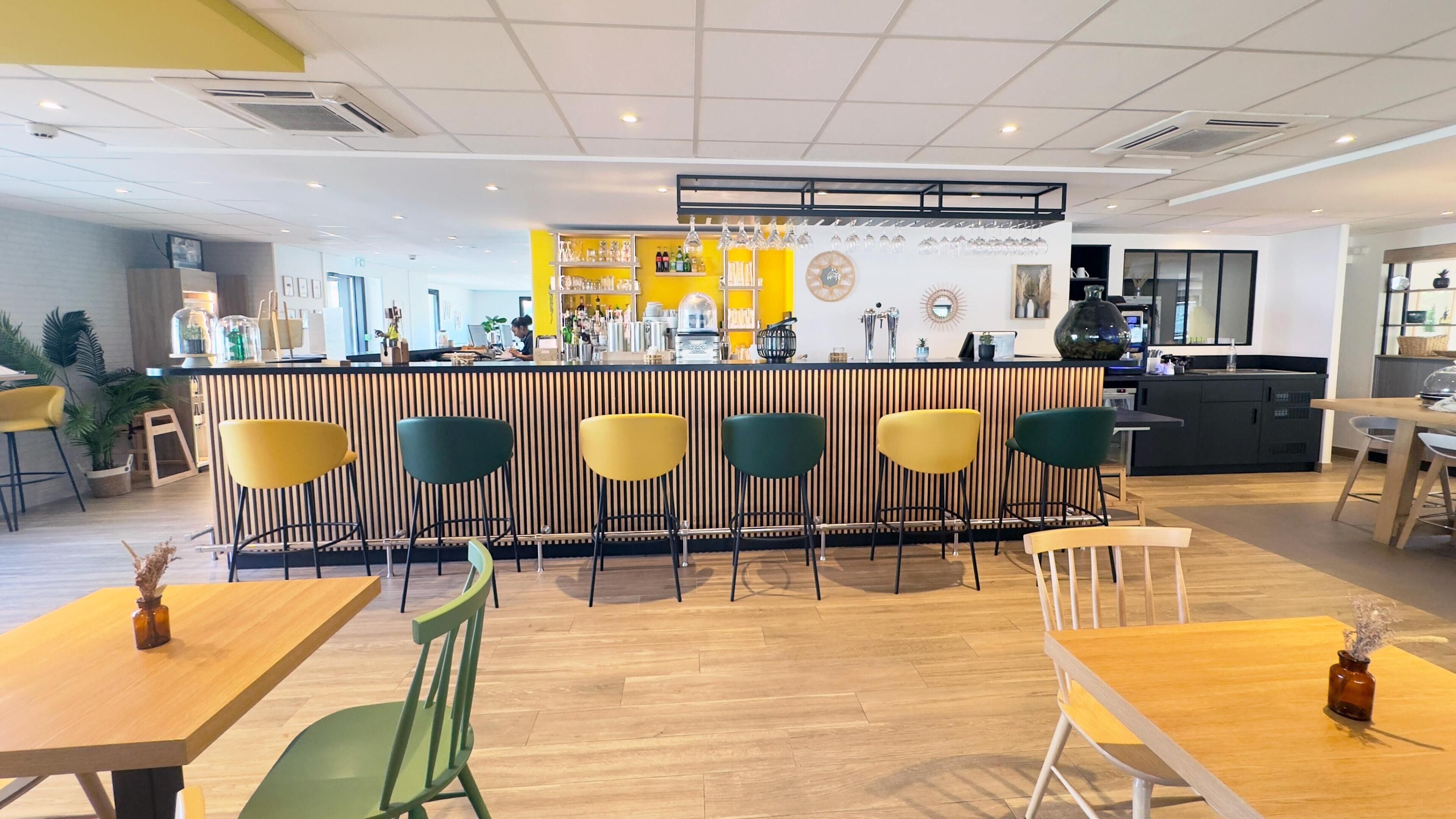 Un café moderno con una zona de bar, suelo de madera y diversas opciones de asientos, incluyendo sillas y mesas.
