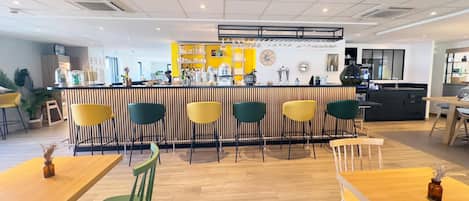 Un café moderno con una zona de bar, suelo de madera y diversas opciones de asientos, incluyendo sillas y mesas.