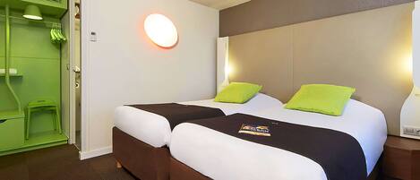 A hotel room with a double bed, two pillows, a bedside table, a nightstand, a green wall, a white door, and a green chair.