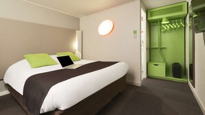 A modern hotel room with a neatly made bed, a green wall-mounted coat rack, and a small green storage unit.