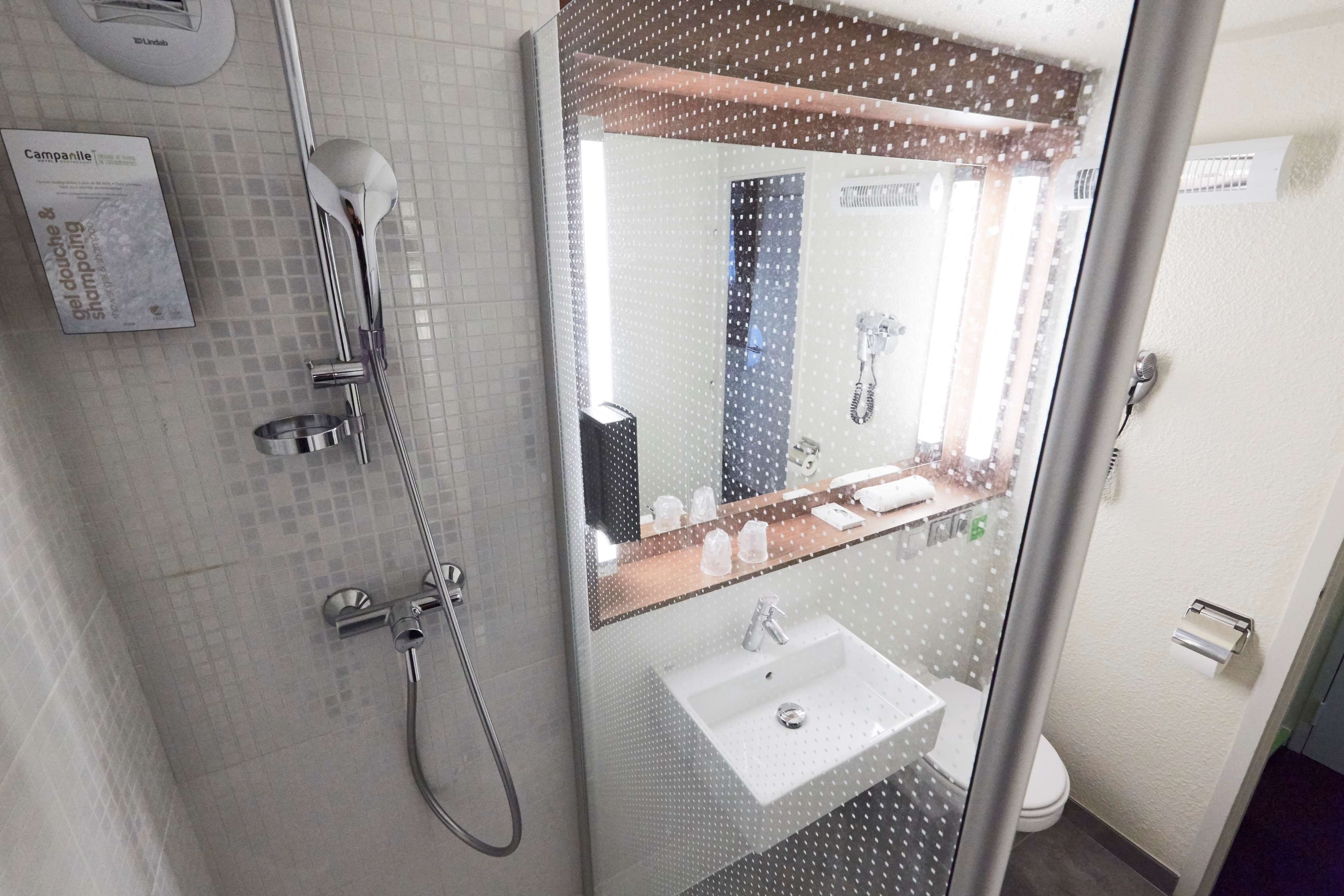 A modern bathroom with a glass shower enclosure, a white sink, and a mirror with a reflection of the bathroom.