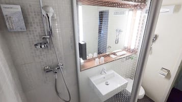 A modern bathroom with a glass shower enclosure, a white sink, and a mirror with a reflection of the bathroom.