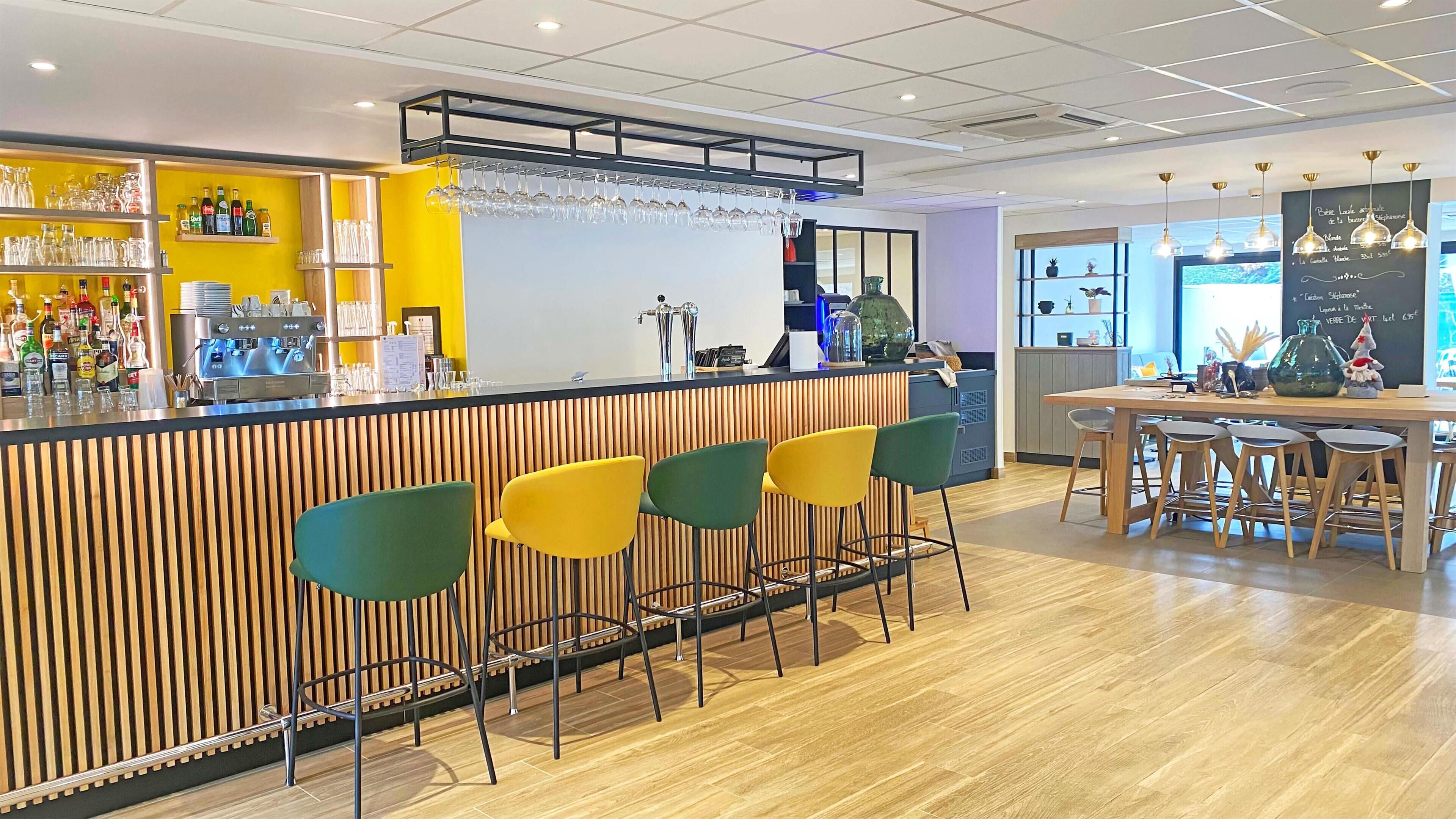 Un espace bar avec un comptoir en bois, des tabourets de bar et un tableau affichant le menu.