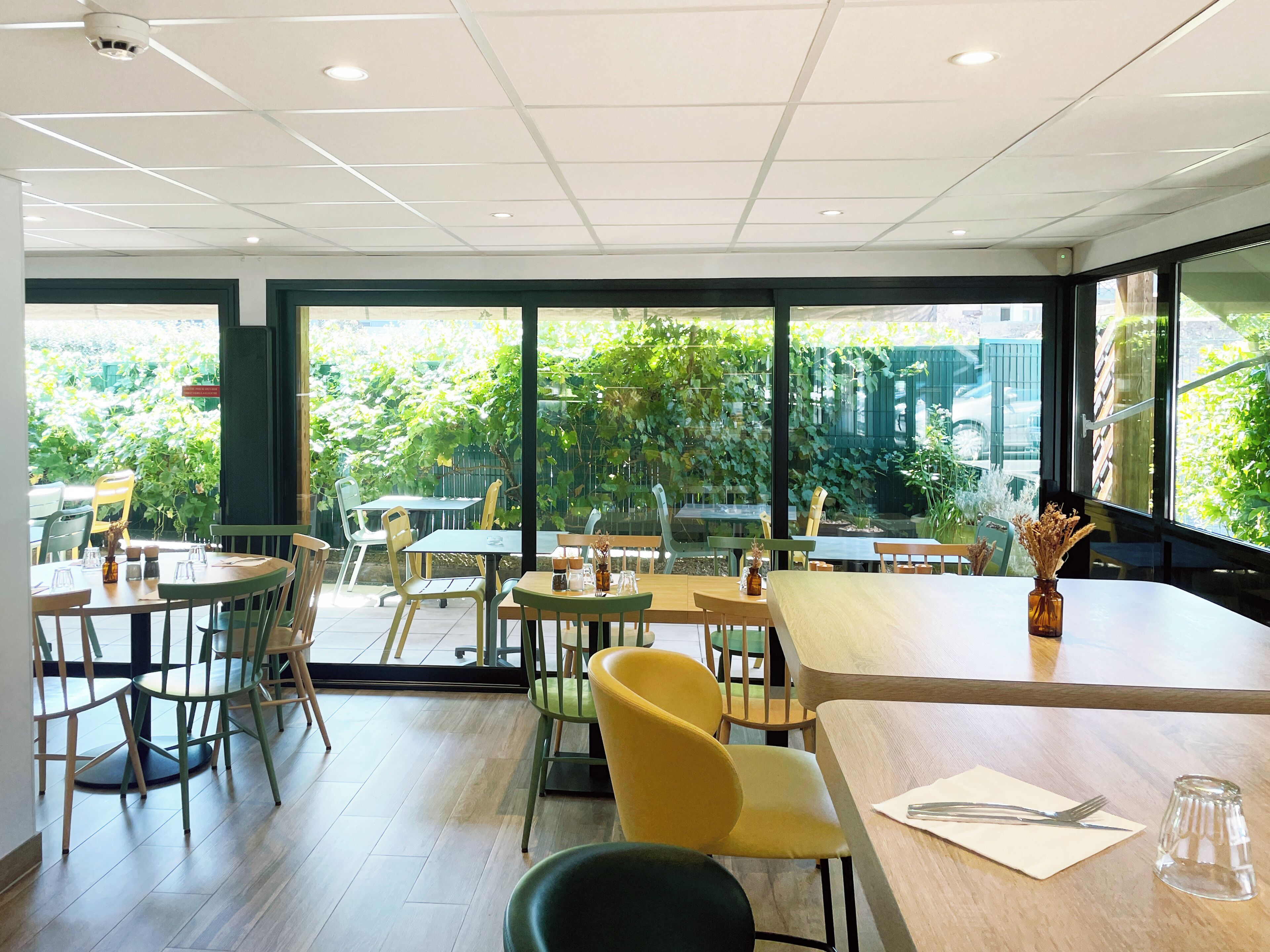 An indoor dining area with tables and chairs, large windows, and a view of greenery outside.