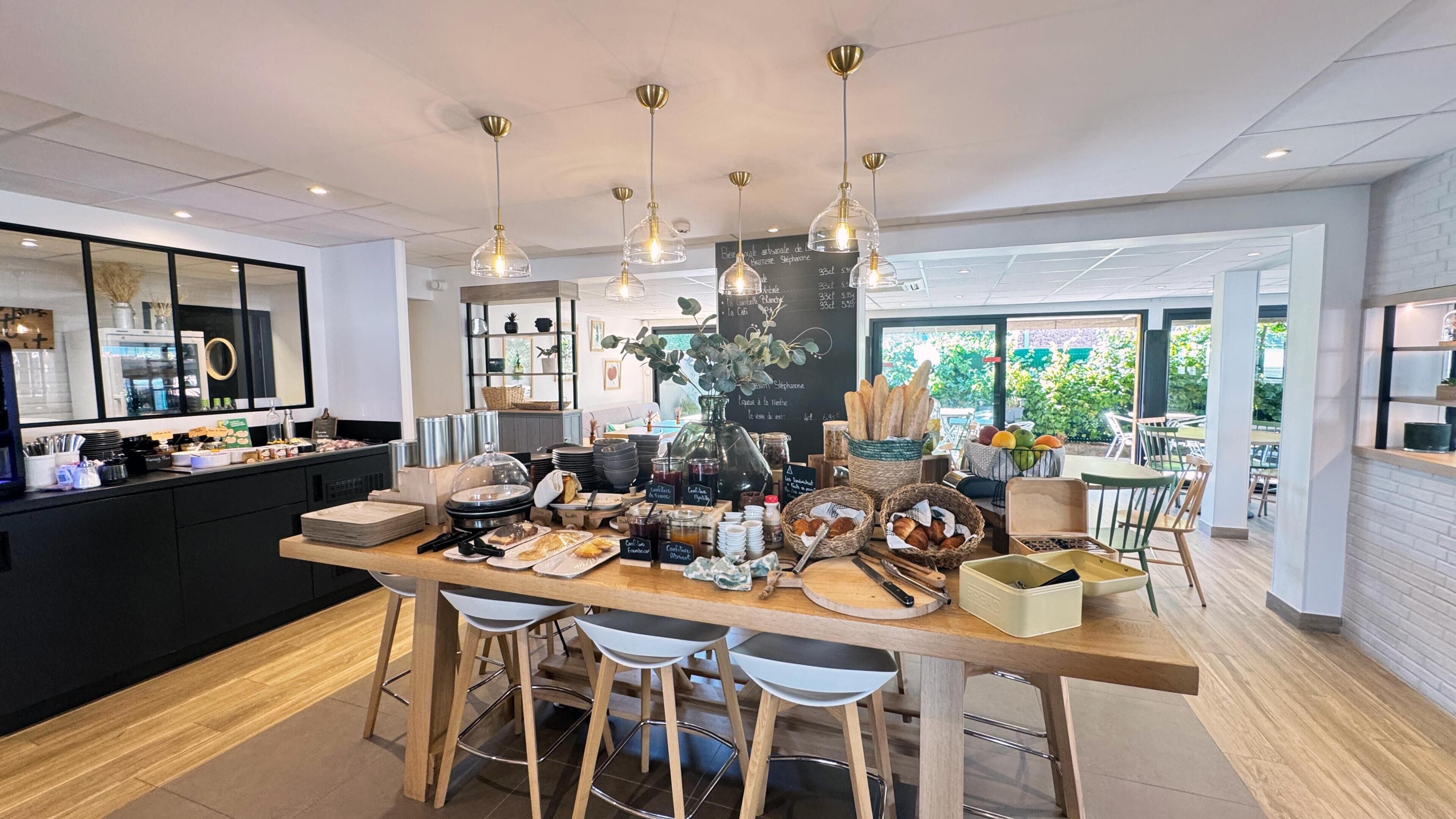 Una cocina moderna con una isla central, taburetes de bar, lámparas colgantes y vistas al exterior.