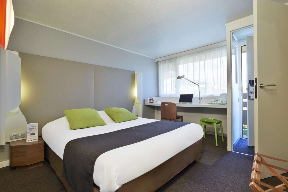A hotel room with a bed, a desk, a chair, and a laptop.