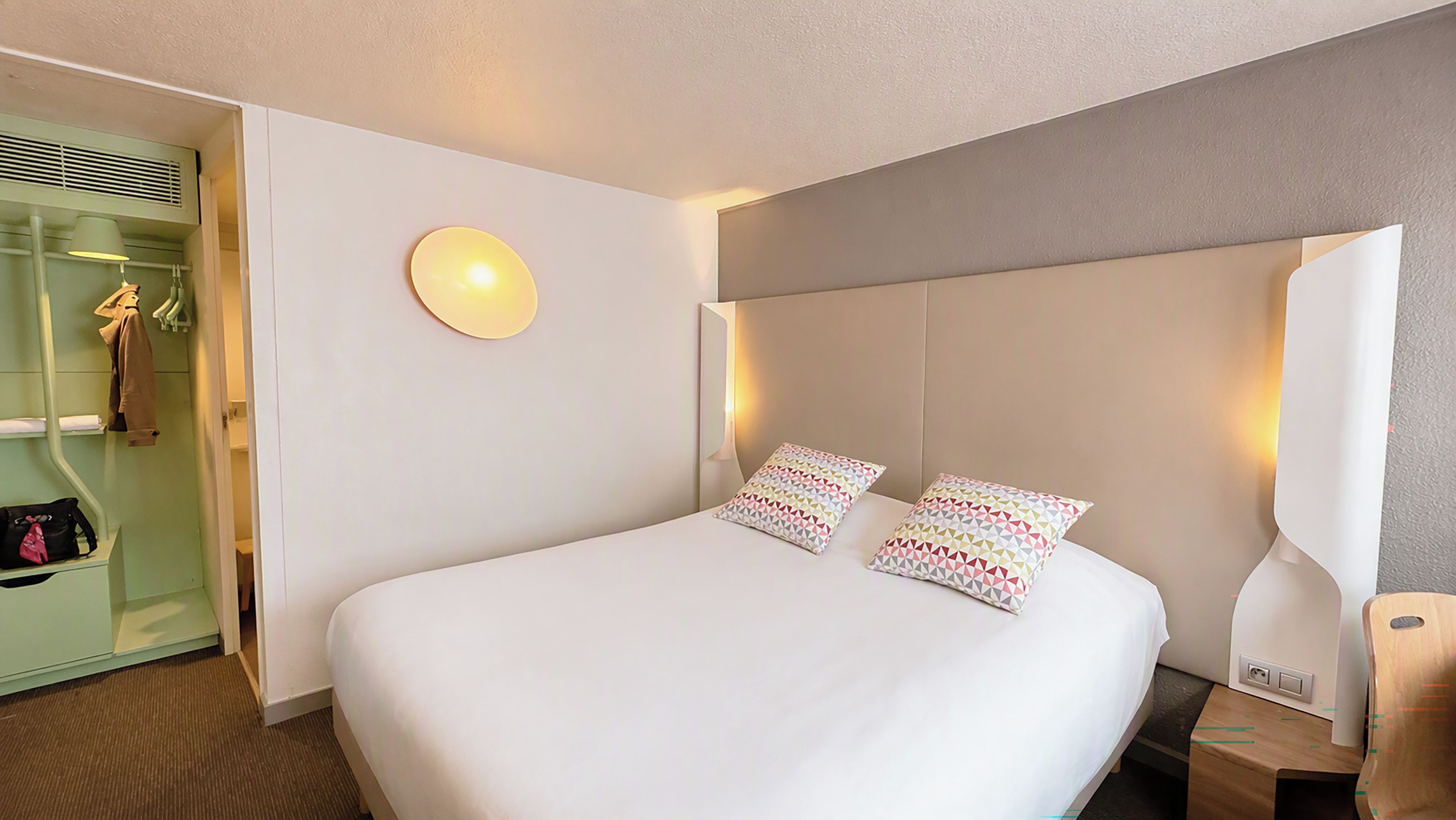 Une chambre d’hôtel avec un grand lit, une table de chevet, une lampe, une armoire et un miroir.