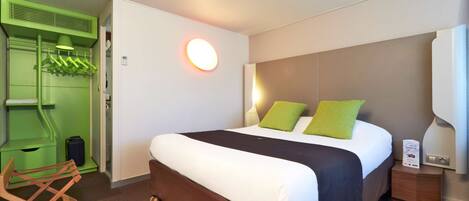 A hotel room with a bed, a green wardrobe, a chair, and a bedside table.