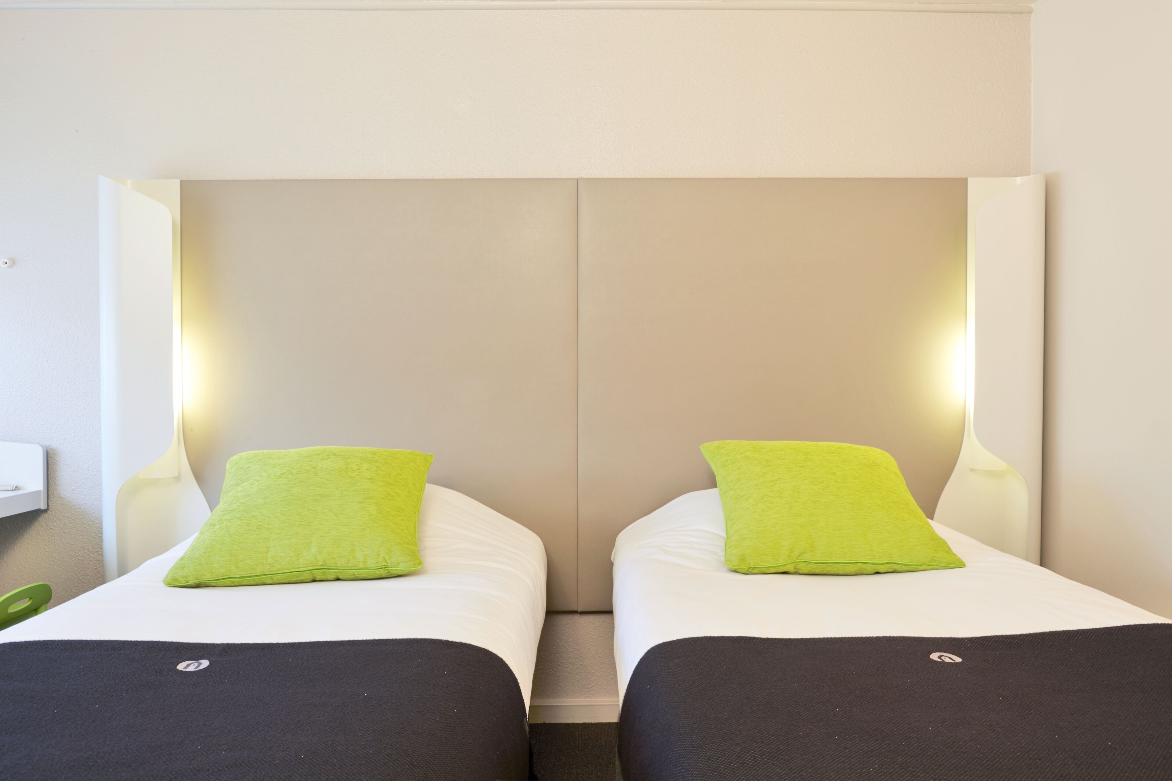 A double room with two beds, each with a green pillow and black bedspread.